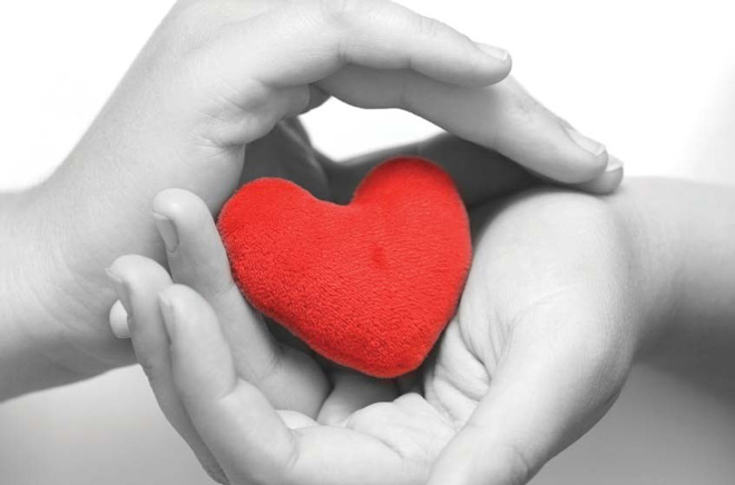 Two hands in black and white photo cradling a bright red heart. 