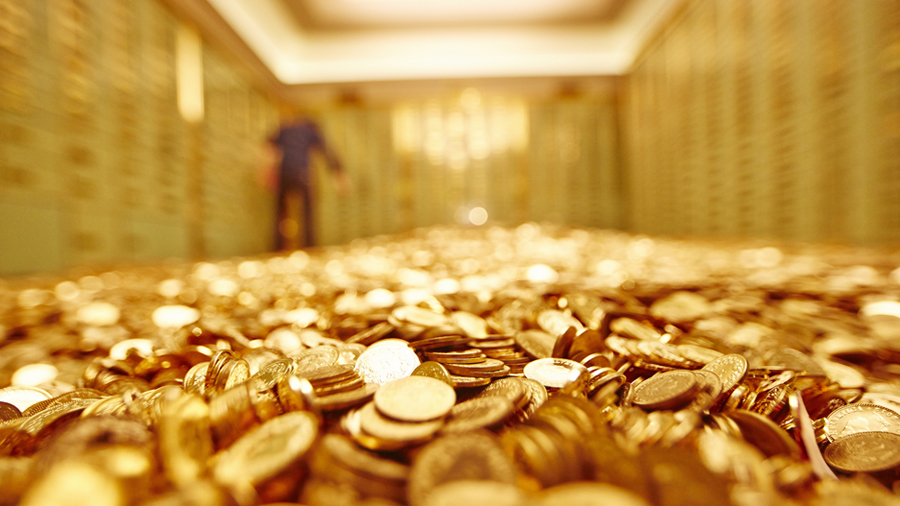 An image of a man standing on a pile of gold coins in a vault.