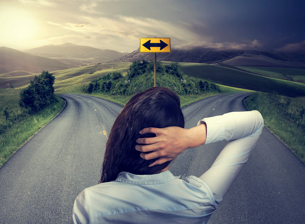 Image of a woman trying to decide which road to go down. One side is bright and sunlit. The other is dark and shadowy.