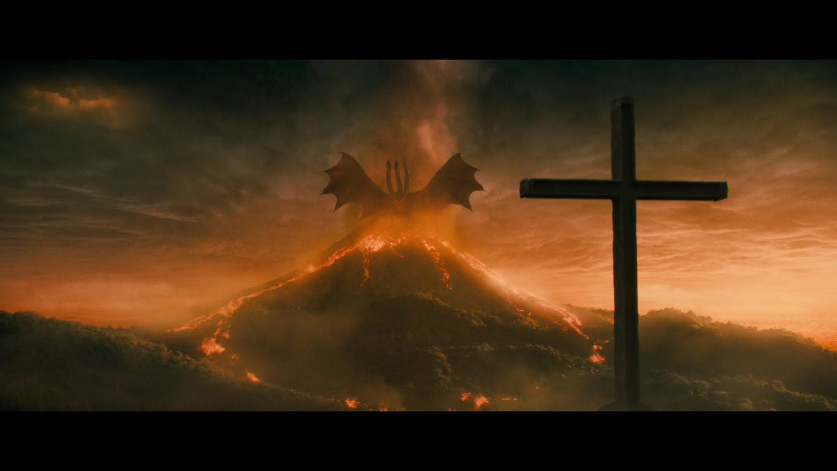 An image of a multi headed beast / dragon sitting on a volcano with a cross in the foreground.