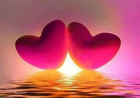 Picture of two hearts in front of a sunrise over the water.