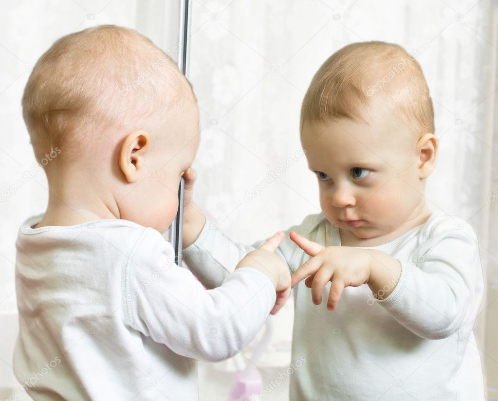 Baby looking critical at its own image in the mirror.
