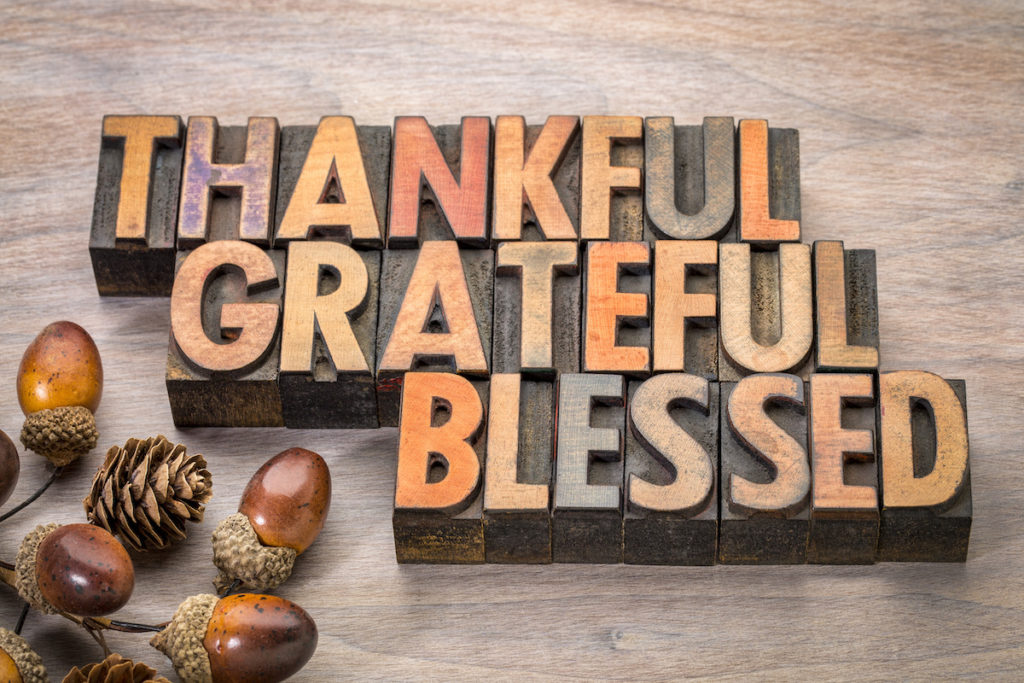 Text "Thankful Grateful Blessed" in wood relief on a table with acorns and pinecones.