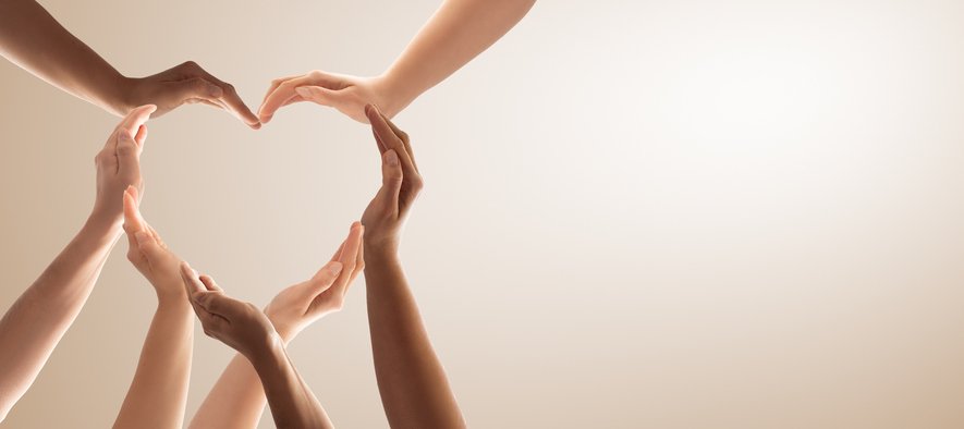 An image of seven hands, all different colors, making the shape of a heart.