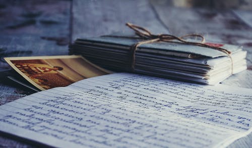 Picture of a handwritten letter amongst a stack of letters. There is a picture of a person slightly obscured by the letter.